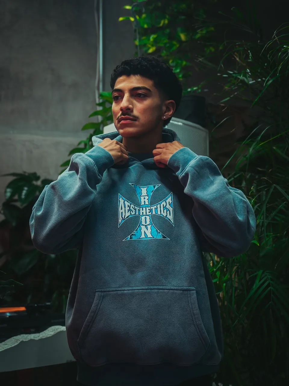 The Blue Cross Hoodie in washed blue, worn with the hood held up