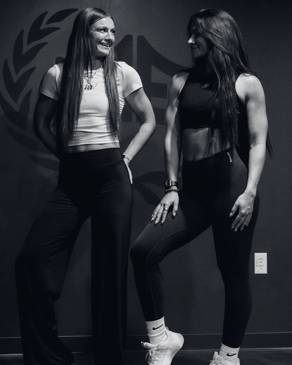 Two athletes in the gym, one in the white ia ruched crop top, one in the black ia crewneck crop tank