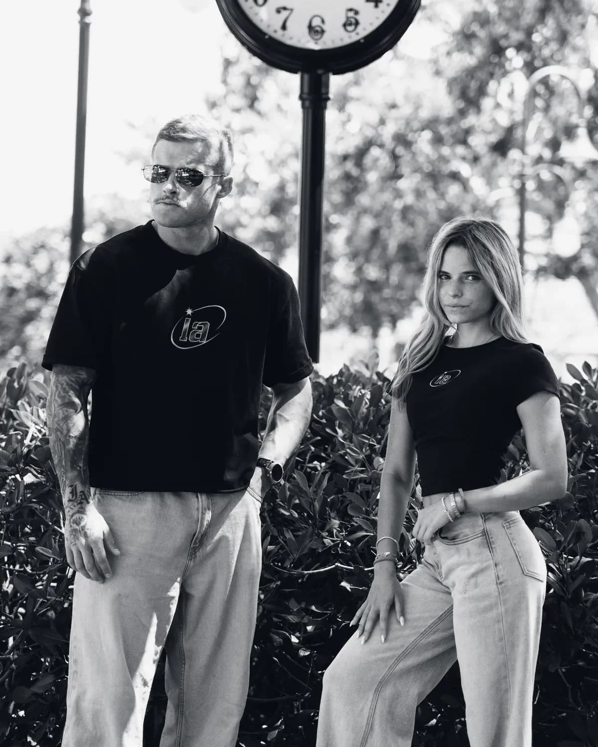 Two athletes wearing the black ia tee and the ia crop tee beside a street clock
